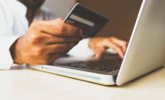 Mann bezahlt eine Rechnung mit seiner Kreditkarte über seinen Laptop